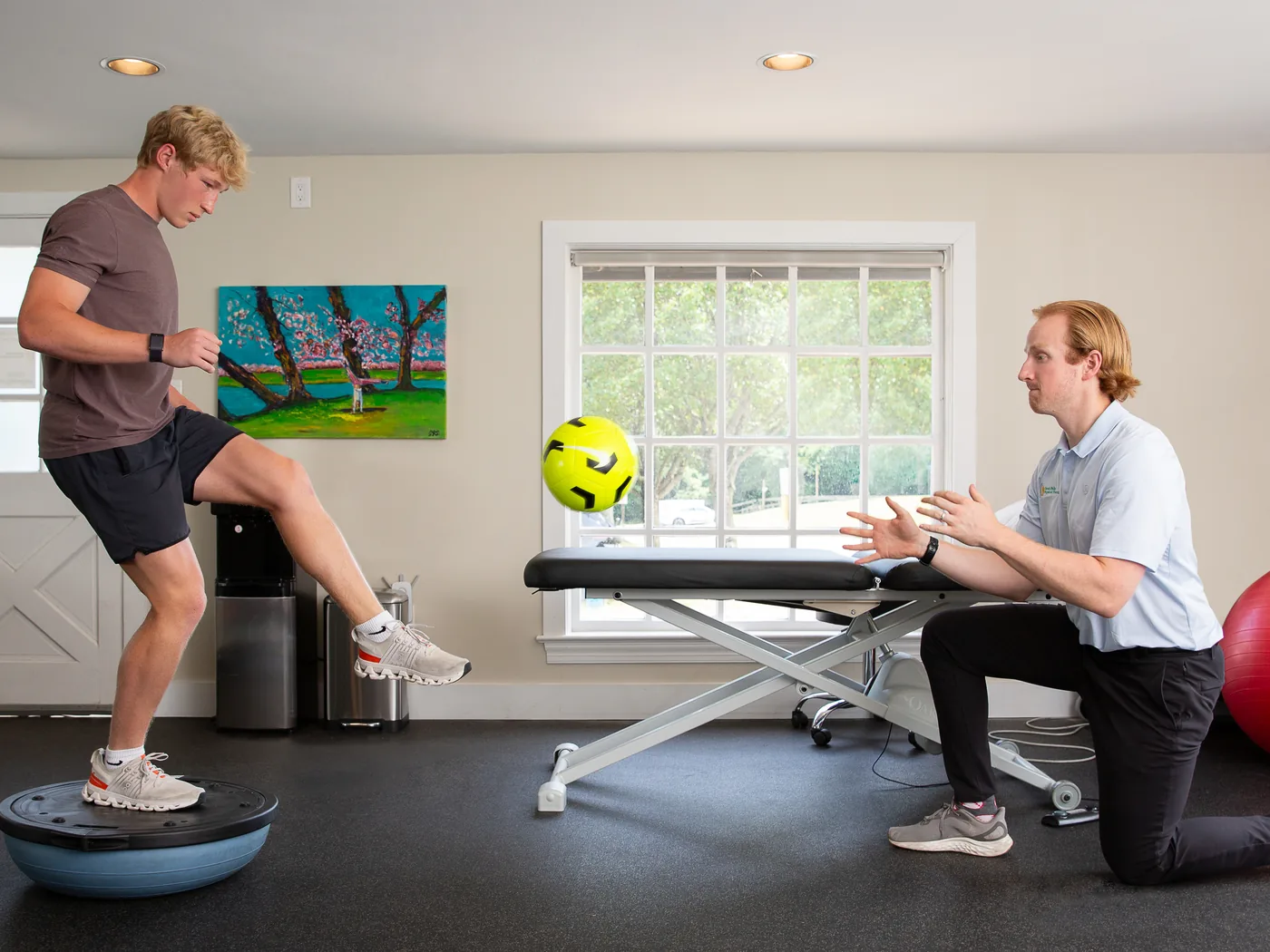 Physical therapist coaching a patient through single-leg balance training on a stability trainer