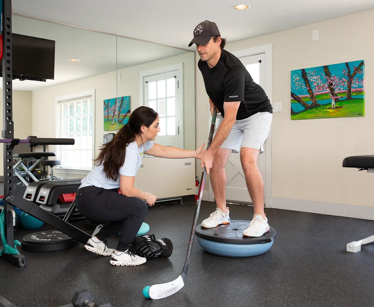 Hockey player training balance on a stability trainer with a therapist during return-to-sport rehabilitation